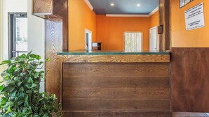 A reception area with a wooden counter, a potted plant, and a sign on the wall. - Econo Lodge Gadsden Area (Grant)