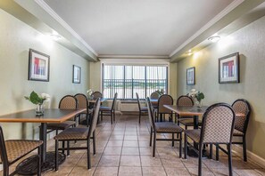 Un espace repas comprenant plusieurs tables et chaises, une grande fenêtre avec des barreaux et des tableaux encadrés accrochés aux murs.