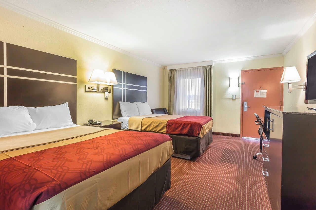 Une chambre d’hôtel avec deux lits, un bureau, une télévision et une porte de salle de bain.