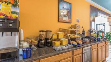 A hotel breakfast area with a coffee machine, fruit containers, and a coffee station.