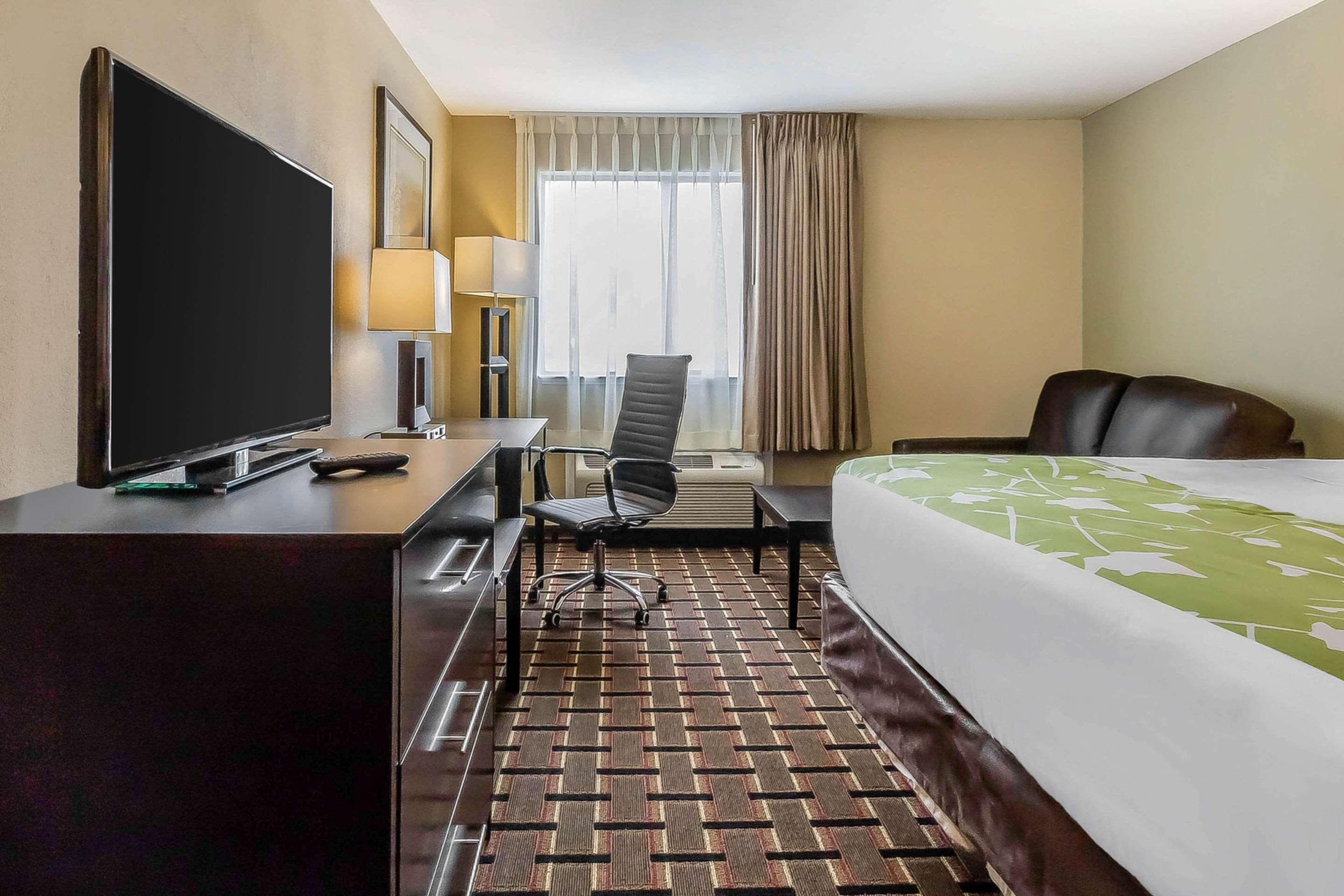 Ein Hotelzimmer mit Bett, Schreibtisch mit Fernseher, Stuhl, Lampe und einem Fenster mit Vorhängen.
