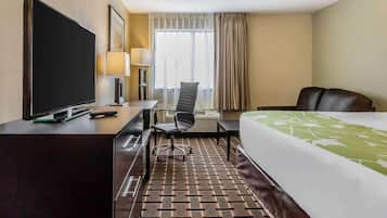 Ein Hotelzimmer mit Bett, Schreibtisch mit Fernseher, Stuhl, Lampe und einem Fenster mit Vorhängen.