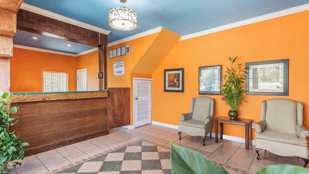 A reception area with a wooden reception desk, two armchairs, a small table with a plant, and framed pictures on the wall. - Econo Lodge Gadsden Area (Grant)