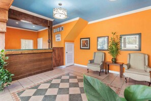 A reception area with a wooden reception desk, two armchairs, a small table with a plant, and framed pictures on the wall. - Econo Lodge Gadsden Area (Grant)
