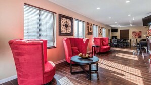 A modern lounge area with red upholstered chairs, a round table with a decorative centerpiece, and a wooden floor. - Econo Lodge Gadsden Area (Grant)
