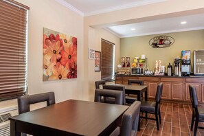 A dining area with a table and chairs, a kitchen with appliances, and a decorative wall piece. - Econo Lodge Gadsden Area (Grant)
