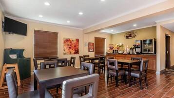 A dining area with multiple tables and chairs, a kitchen area with appliances, and a television mounted on the wall.