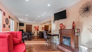 A spacious living room with a red sofa, a fireplace, a TV mounted on the wall, and a dining area in the background. - Econo Lodge Gadsden Area (Grant)