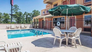 A swimming pool with lounge chairs and a table, surrounded by a building with balconies and a fence. - Econo Lodge Gadsden Area (Grant)