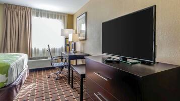 Habitación de hotel con cama, escritorio, silla, televisor y alfombra estampada.