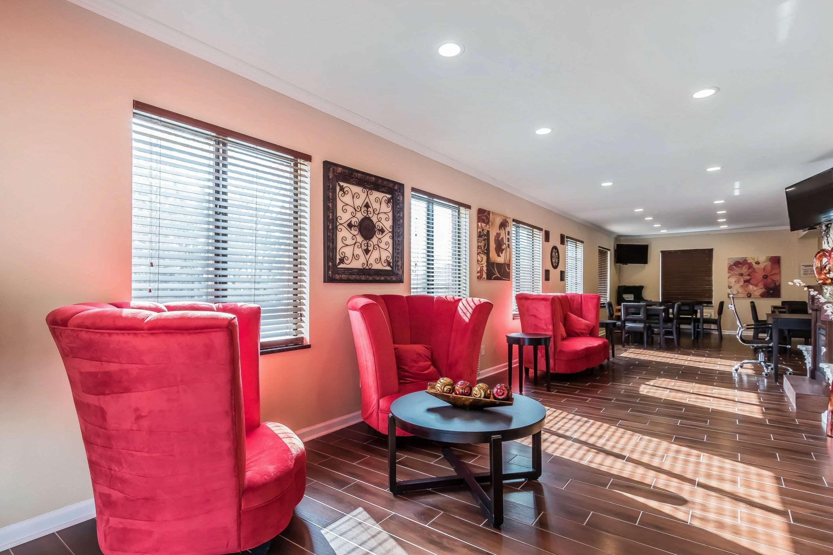 Un área de descanso moderna con sillones tapizados de color rojo, una mesa redonda con un centro de mesa decorativo y suelo de madera.