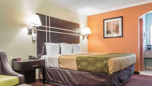 A hotel room with a bed, bedside table, lamp, and a painting on the wall. - Econo Lodge Gadsden Area (Grant)