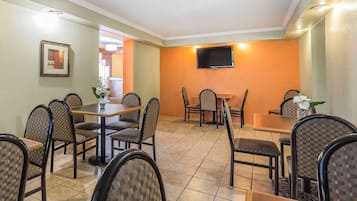 A dining area with multiple tables and chairs, a flat-screen TV mounted on the wall, and a framed picture on the wall.