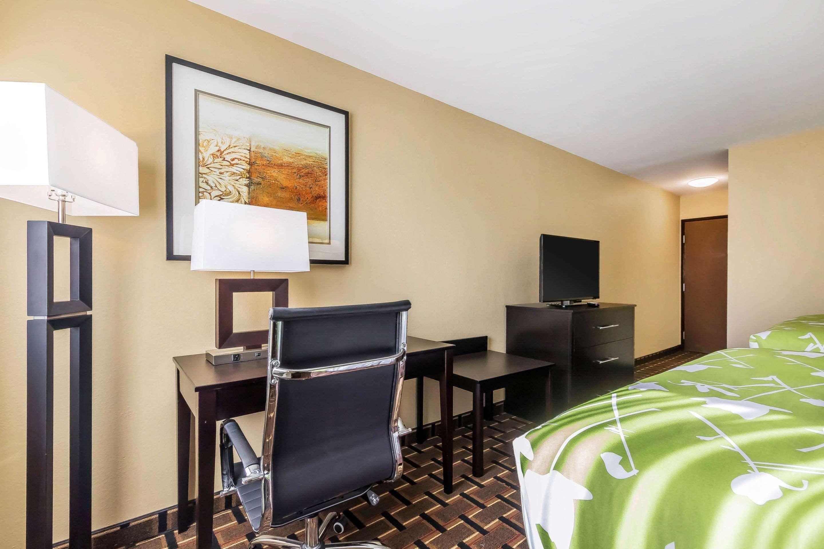 A hotel room with a bed, a desk with a chair, a television, and a framed picture on the wall.