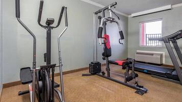 Une salle de sport équipée de divers appareils d’exercice, une fenêtre avec vue et un tapis de course.