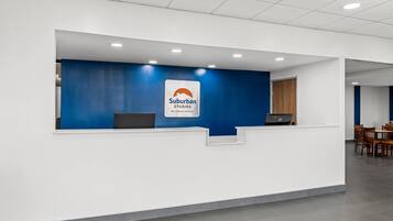 Un mostrador de recepción con una pared azul decorativa, una computadora portátil y un cartel de Suburban Studios by Choice Hotels.