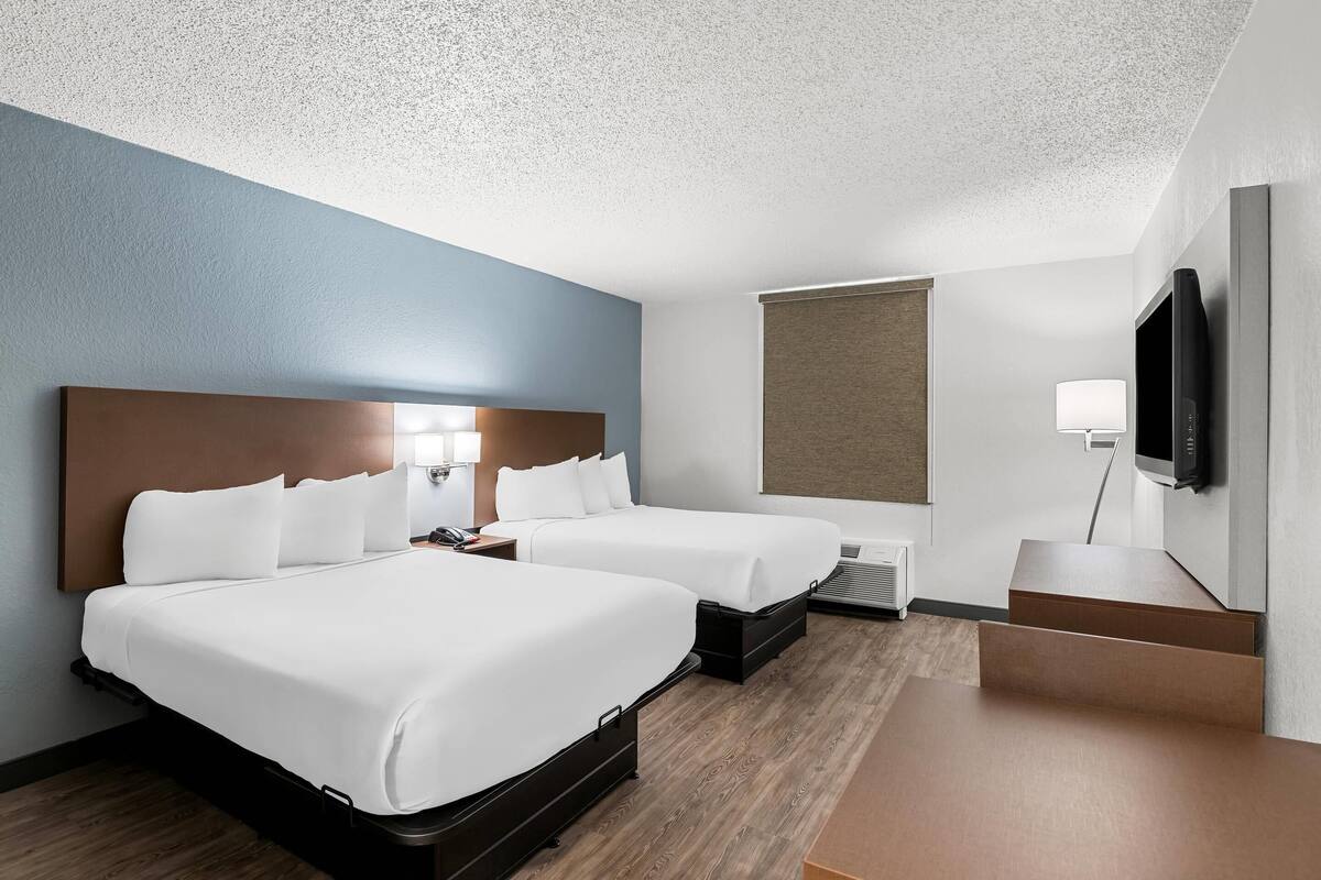 A hotel room with two beds, a flat-screen TV, a desk, and a window.