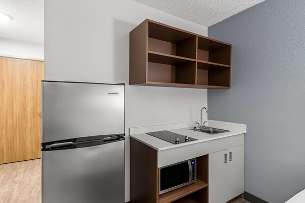 A compact kitchen with a stainless steel refrigerator, a microwave, and a sink with a countertop. - Suburban Studios Chester I-95 (Chester)