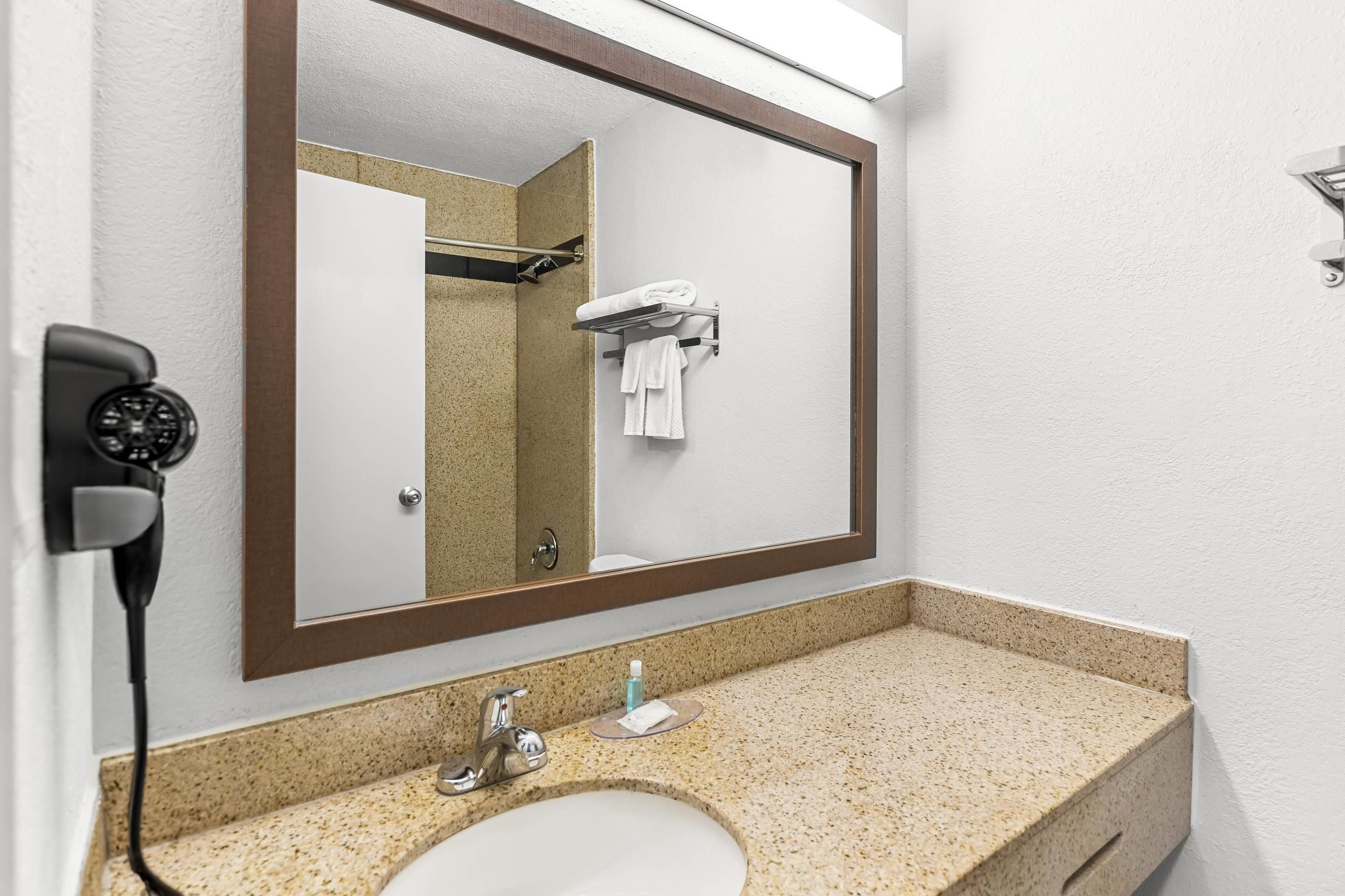 A bathroom with a large mirror, a sink, a towel rack, and a hairdryer plugged in.