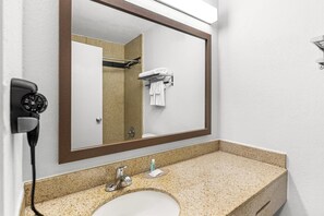 A bathroom with a large mirror, a sink, a towel rack, and a hairdryer plugged in. - Suburban Studios Chester I-95 (Chester)
