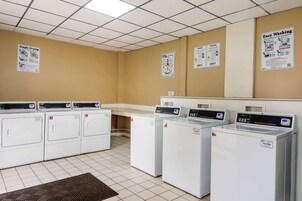Una sala de lavandería con varias lavadoras, piso de baldosas y carteles informativos en las paredes.