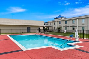 A swimming pool with a red and white tiled deck, surrounded by a black fence, and a building with a blue roof in the background.