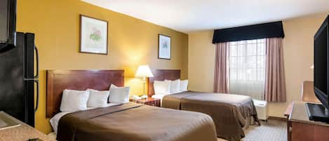 A hotel room with two beds, a refrigerator, a TV, and a window with curtains.