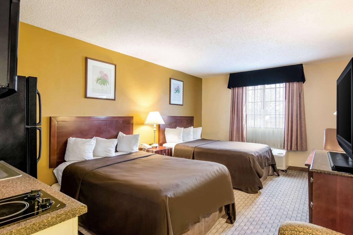 A hotel room with two beds, a refrigerator, a TV, and a window with curtains.