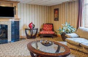 Una sala de estar con chimenea, un sofá, un sillón rojo, una mesa de centro redonda y un televisor.