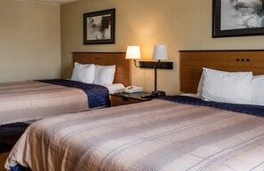 A hotel room with two beds, a nightstand with a lamp, and a framed picture on the wall.