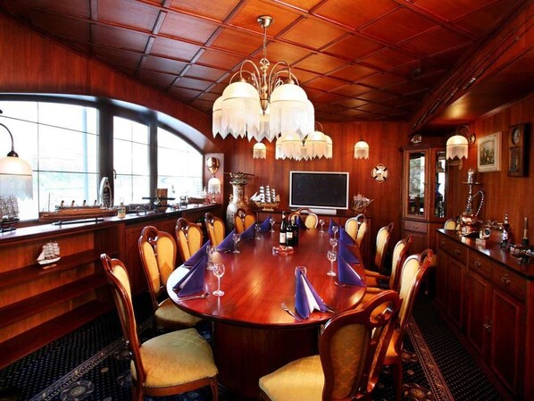 A conference room with a large wooden table, chairs, a chandelier, and a television. - Botel Albatros (Prague)