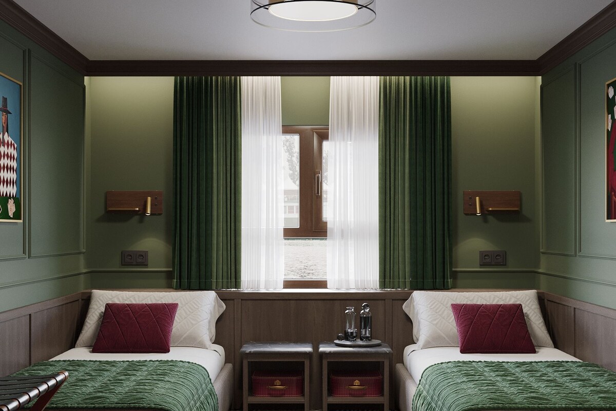 A hotel room with two beds, a window with curtains, a small table with a lamp, and a patterned floor.