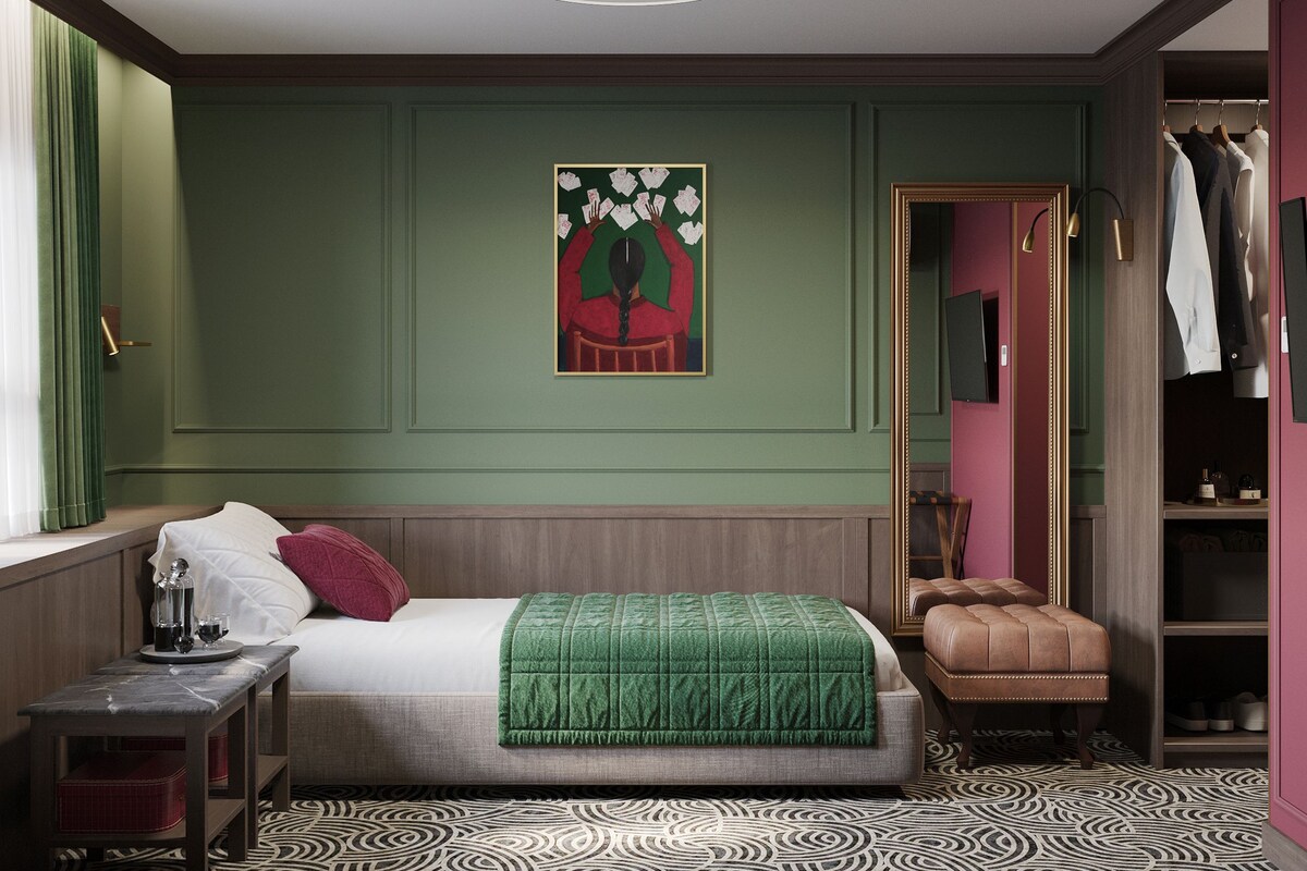 Een slaapkamer met een bed, nachtkastje en een groene muur met een kunstwerk in een lijst.