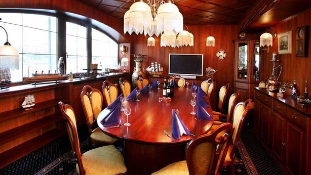 A conference room with a large wooden table, chairs, a chandelier, and a television. - Botel Albatros (Prague)