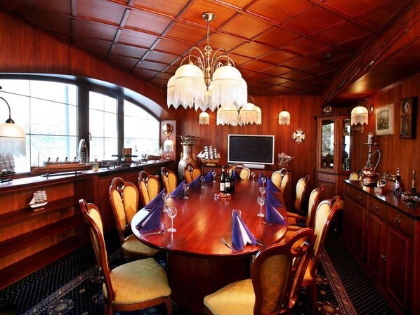 A conference room with a large wooden table, chairs, a chandelier, and a television. - Botel Albatros (Prague)