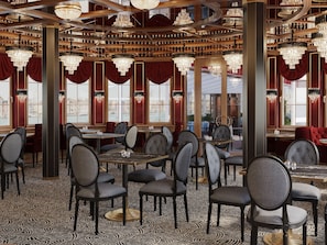 L’intérieur d’un restaurant, avec de nombreuses tables et chaises, des lustres et de grandes fenêtres ornées de rideaux.