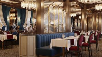 A restaurant with a blue booth seating area, multiple tables with red upholstered chairs, and chandeliers.