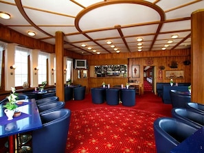 Habitación de hotel con alfombra roja, paredes de madera y una zona de bar con taburetes y una televisión.