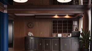 A reception area with a curved dark wood desk, a ship's wheel decoration, and a bookshelf with various items. - Botel Albatros (Prague)