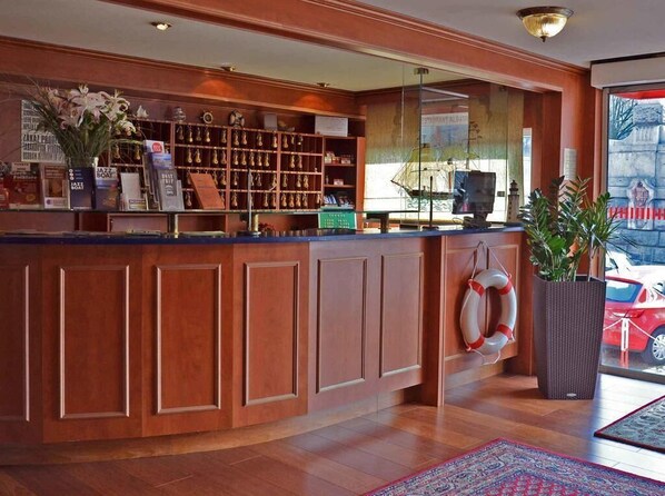 A reception area with a wooden counter, shelves with awards, a life preserver, and a large potted plant. - Botel Albatros (Prague)