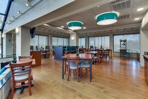A spacious indoor area with multiple wooden tables and chairs, large windows, and a high ceiling with exposed beams. - Pear Tree Inn Airport St. Louis - St. Ann (St. Ann)