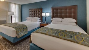 Habitación de hotel con dos camas, una mesita de noche, una lámpara y una ventana con cortinas.