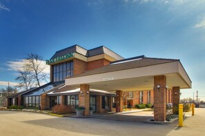 Hotel com entrada coberta, placa visível e área de estacionamento.