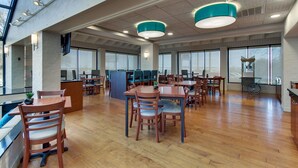 A spacious indoor area with multiple wooden tables and chairs, large windows, and a high ceiling with exposed beams. - Pear Tree Inn Airport St. Louis - St. Ann (St. Ann)