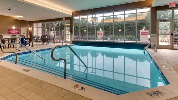 An indoor swimming pool with clear glass walls, a lifeguard chair, and a no diving allowed sign. - Drury Plaza Hotel Richmond (Glen Allen)