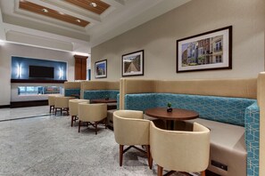 A modern hotel lobby with seating areas, a television, framed pictures on the walls, and a marble floor. - Drury Plaza Hotel Richmond (Glen Allen)