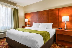 A hotel room with a large bed, wooden headboard, two bedside tables with lamps, and a window with curtains. - Drury Plaza Hotel Richmond (Glen Allen)