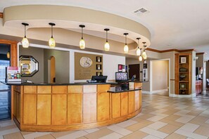 A hotel reception area with a curved wooden counter, multiple pendant lights, a clock, and a sign indicating 'Comfort Suites'. - Drury Plaza Hotel Richmond (Glen Allen)