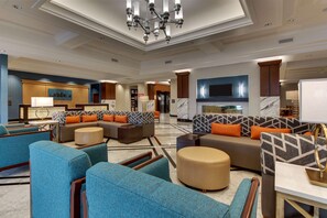 A spacious lobby with multiple seating areas, a central chandelier, and a modern kitchen in the background. - Drury Plaza Hotel Richmond (Glen Allen)
