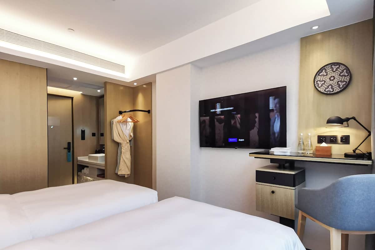 A hotel room with two beds, a TV, a desk with a lamp, and a robe hanging on a rack.